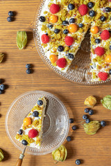 Moostorte aus grünem Biscuit mit Quark, Sahne, Früchte, Blaubeere, Himbeere, Physalis auf Holz