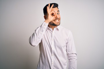 Fototapeta premium Young handsome man wearing elegant shirt standing over isolated white background doing ok gesture with hand smiling, eye looking through fingers with happy face.