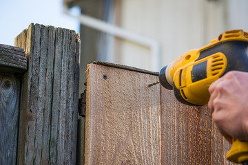 Construction worker carpenter drilling hole in fence gate board with electric drill