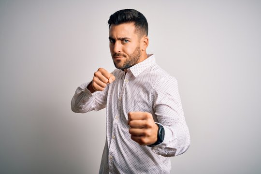 Young handsome man wearing elegant shirt standing over isolated white background Punching fist to fight, aggressive and angry attack, threat and violence