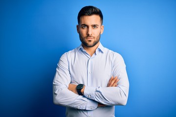Young handsome man wearing elegant shirt standing over isolated blue background skeptic and nervous, disapproving expression on face with crossed arms. Negative person.