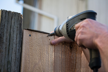 construction worker carpenter driving inserting screw in fence gate board with drill