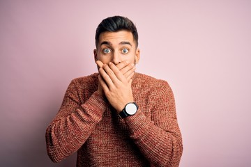 Young handsome man wearing casual sweater standing over isolated pink background shocked covering mouth with hands for mistake. Secret concept.