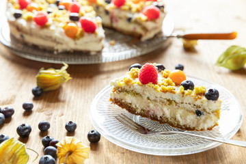 Moostorte aus grünem Biscuit mit Quark, Sahne, Früchte, Blaubeere, Himbeere, Physalis auf Holz