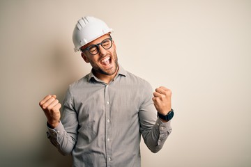 Young architect man wearing builder safety helmet over isolated background very happy and excited...