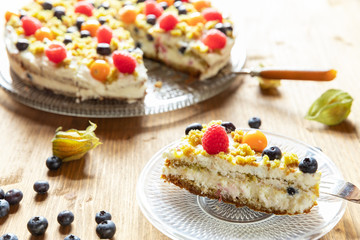Moostorte aus grünem Biscuit mit Quark, Sahne, Früchte, Blaubeere, Himbeere, Physalis auf Holz