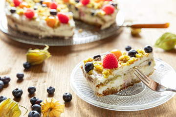 Moostorte aus grünem Biscuit mit Quark, Sahne, Früchte, Blaubeere, Himbeere, Physalis auf Holz