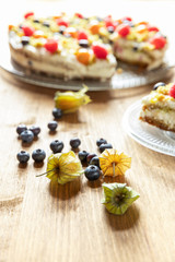 Moostorte aus grünem Biscuit mit Quark, Sahne, Früchte, Blaubeere, Himbeere, Physalis auf Holz