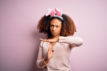 Young african american woman with afro hair wearing bunny ears over pink background Doing time out gesture with hands, frustrated and serious face