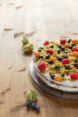 Moostorte aus grünem Biscuit mit Quark, Sahne, Früchte, Blaubeere, Himbeere, Physalis auf Holz