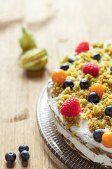 Moostorte aus grünem Biscuit mit Quark, Sahne, Früchte, Blaubeere, Himbeere, Physalis auf Holz
