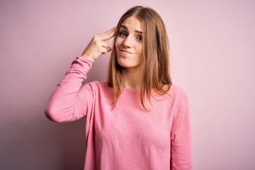 Young beautiful redhead woman wearing casual sweater over isolated pink background Shooting and killing oneself pointing hand and fingers to head like gun, suicide gesture.