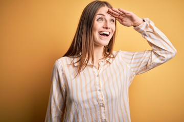 Young beautiful redhead woman wearing casual striped shirt over isolated yellow background very...
