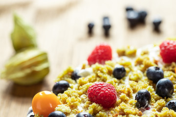 Moostorte aus grünem Biscuit mit Quark, Sahne, Früchte, Blaubeere, Himbeere, Physalis auf Holz