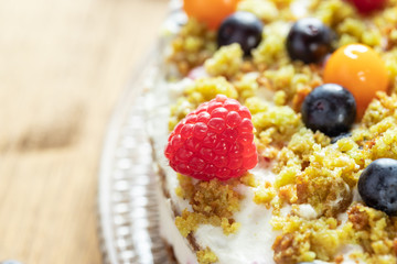 Moostorte aus grünem Biscuit mit Quark, Sahne, Früchte, Blaubeere, Himbeere, Physalis auf Holz