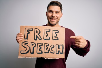 Young man with blue eyes holding banner on protest for free speech asking for free communication very happy pointing with hand and finger