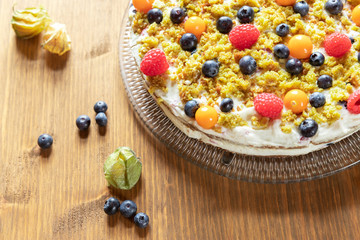 Moostorte aus grünem Biscuit mit Quark, Sahne, Früchte, Blaubeere, Himbeere, Physalis auf Holz