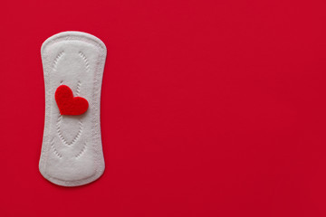 Menstrual pad with red sequins in the shape of a heart on a red background, top view, miniature of the menstrual period