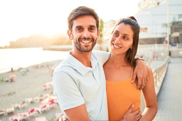 Obraz premium Young beautiful couple on vacation smiling happy and confident. Standing with smile on face hugging at the beach