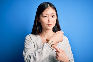 Young beautiful asian woman wearing casual sweater standing over blue isolated background In hurry...