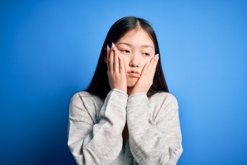 Young beautiful asian woman wearing casual sweater standing over blue isolated background Tired hands covering face, depression and sadness, upset and irritated for problem