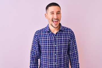 Young handsome man standing over isolated background winking looking at the camera with sexy expression, cheerful and happy face.