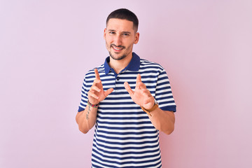 Fototapeta premium Young handsome man wearing nautical striped t-shirt over pink isolated background disgusted expression, displeased and fearful doing disgust face because aversion reaction. With hands raised. Annoying