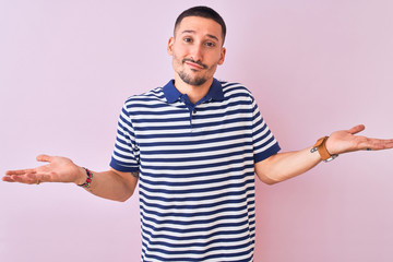 Fototapeta premium Young handsome man wearing nautical striped t-shirt over pink isolated background clueless and confused expression with arms and hands raised. Doubt concept.