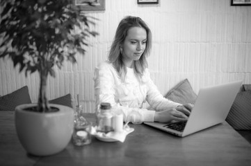 Fototapeta premium Beautiful young freelancer woman using laptop computer sitting at cafe table. Happy smiling girl working online or studying and learning while using notebook. Freelance work, business people concept