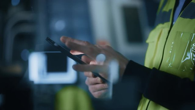 Professional Engineer Wearing Safety Vest Uses Digital Tablet Computer. Slow Motion Focus on Hands Using Gestures. Working in Industrial Facility with High Tech Machinery.