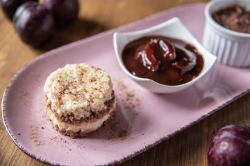 Grießflammerie aus Grieß mit Kakao und Sahne mit gekochtem Pflaumenmus und Pflaumen auf rosa ovalem Teller und Holz