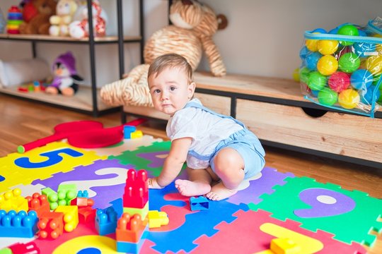 Beautiful toddler sitting on puzzle carpet playing with building blocks at kindergarten