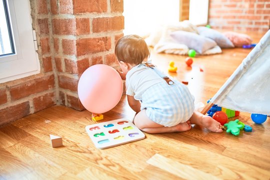 Adorable toddler crawling around lots of toys at kindergarten