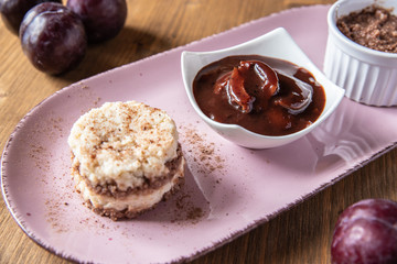 Grießflammerie aus Grieß mit Kakao und Sahne mit gekochtem Pflaumenmus und Pflaumen auf rosa ovalem Teller und Holz