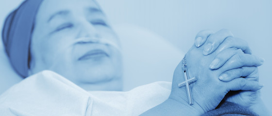 Fototapeta premium christian cross in hands of cancer patient wearing headscarf during chemotherapy treatment lying on bed in hospital praying and worship for hope, in monotone