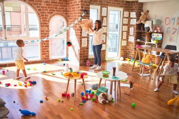 Beautiful teacher and toddlers playing basketball using balls and wicker basket  around lots of toys at kindergarten