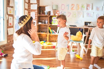 Beautiful teacher and toddlers playing with king crown around lots of toys at kindergarten