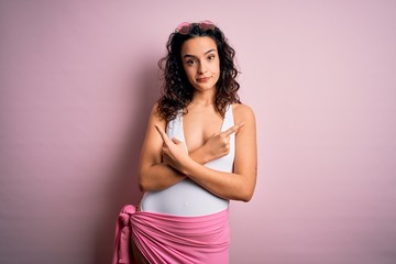 Obraz premium Beautiful woman with curly hair on vacation wearing white swimsuit over pink background Pointing to both sides with fingers, different direction disagree
