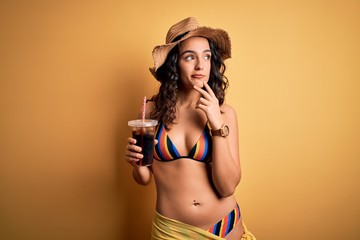 Young beautiful woman with curly hair on vacation wearing bikini drinking cola beverage serious...