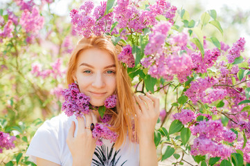 Obraz na płótnie Canvas Picture of young caucasian woman with red hair smiles and smells lilac in the garden