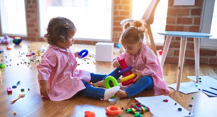 Adorable toddlers wearing uniform sitting on the floor building pyramid using hoops at kindergarten
