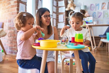 Young beautiful teacher and toddlers playing meals using plastic food and cutlery toy at...