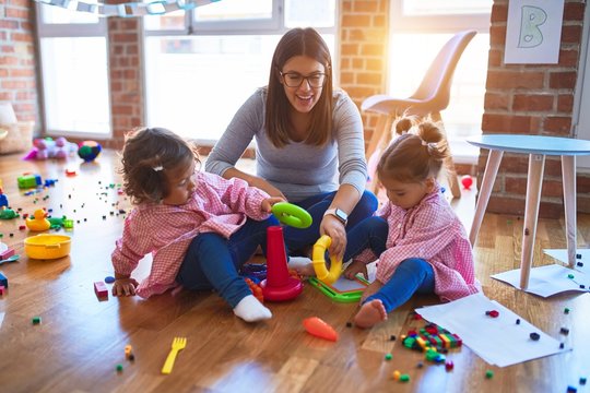 Young beautiful teacher and toddlers wearing uniform building pyramid using hoops at kindergarten