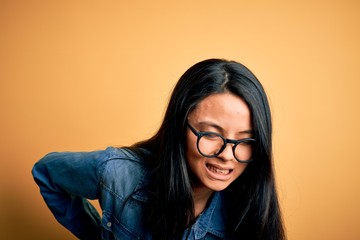 Young beautiful chinese woman wearing casual denim shirt over isolated yellow background Suffering of backache, touching back with hand, muscular pain