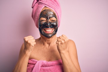 Middle age brunette woman wearing beauty black face mask over isolated pink background excited for success with arms raised and eyes closed celebrating victory smiling. Winner concept.