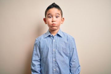 Young little boy kid wearing elegant shirt standing over isolated background puffing cheeks with funny face. Mouth inflated with air, crazy expression.