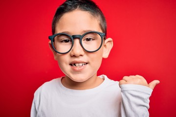 Young little smart boy kid wearing nerd glasses over red isolated background pointing and showing with thumb up to the side with happy face smiling