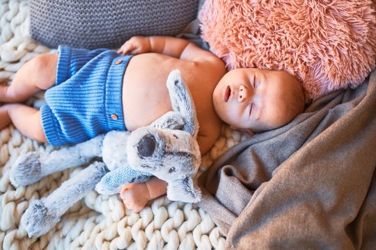 Adorable baby lying down on the sofa over blanket at home. Newborn relaxing and resting comfortable with doll