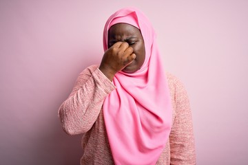 Young african american plus size woman wearing muslim hijab over isolated pink background tired rubbing nose and eyes feeling fatigue and headache. Stress and frustration concept.