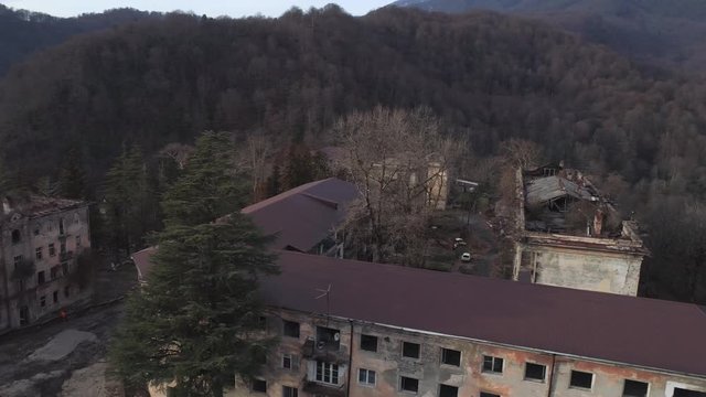 Old settlement at the top of mountain hill. Shot. Aerial view of the old abandoned residential buildings surrounded by mountains with trees.
